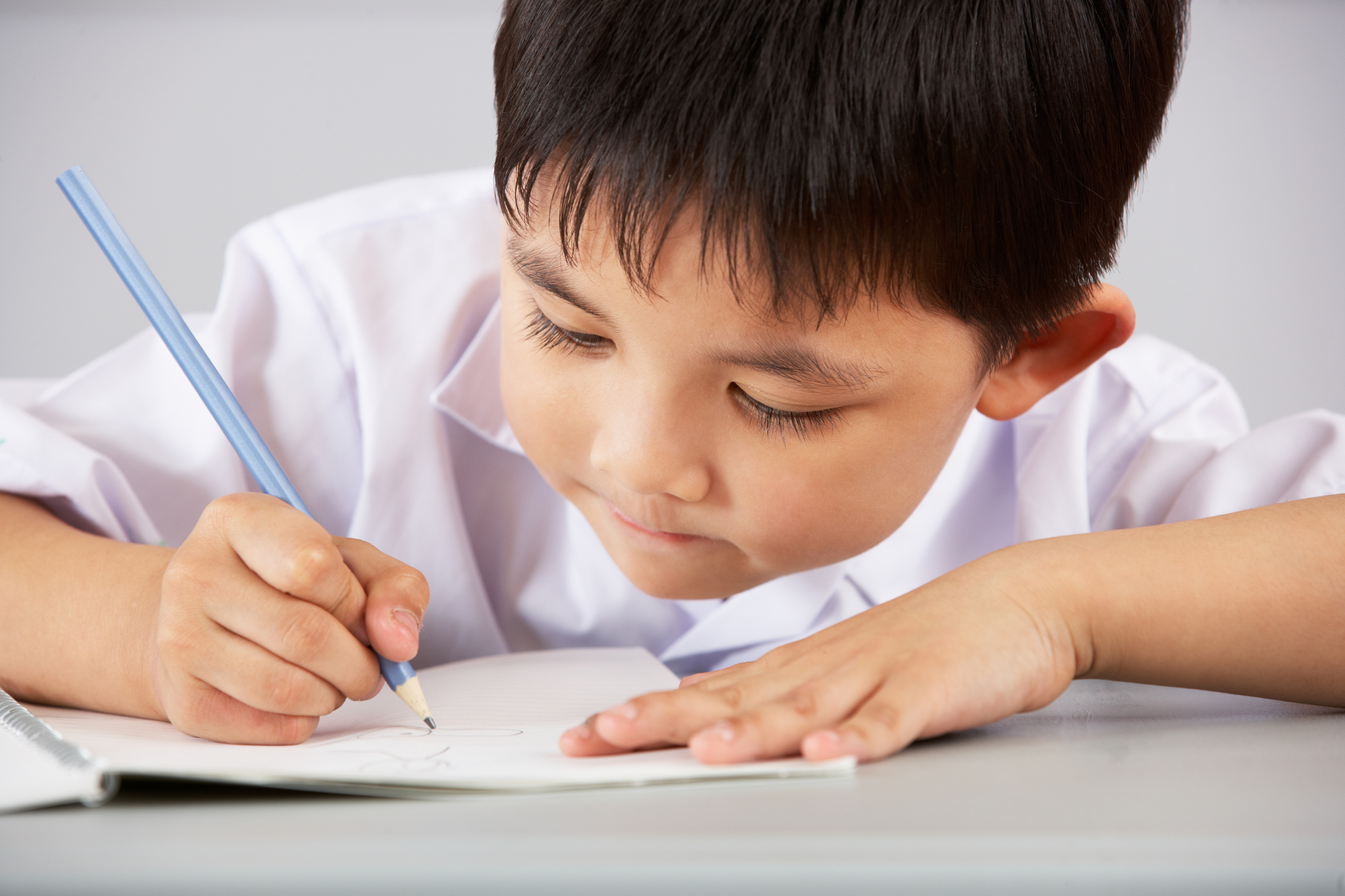 An image of a young Chinese student writing in a notebook. 