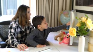 Preschool boy and mother interact with tutor during online language lesson.