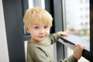 Blonde toddler boy touching window sill.